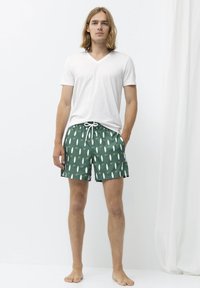 Bílý tričko s véčkovým výstřihem v kombinaci se zelenými plavkovými šortkami s vzorem surfboardu, elastickým pasem a bočními kapsami.