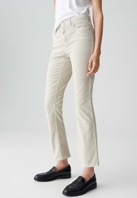 Beige rechte jeans met een subtiele textuur en voorzakken, gecombineerd met zwarte loafers van glad leer.