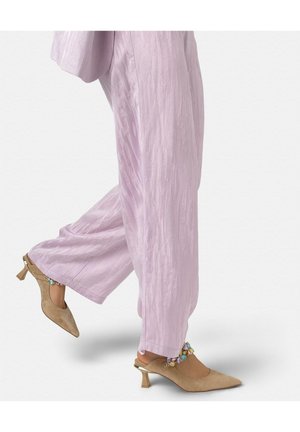 Piernas con pantalones anchos color lila claro que llevan tacones slingback beige de punta puntiaguda con correas de tobillo coloridas con cuentas.