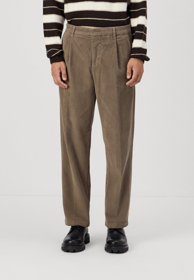 Brown corduroy trousers with a loose fit, featuring front pleats and a textured surface. Paired with black leather shoes.