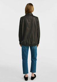 Czarna lekka kurtka z kołnierzem, z mankietami, elastycznym dołem, zestawiona z niebieskimi dżinsami prostymi i czarnymi butami wsuwanymi.