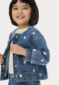Giacca di denim con lavaggio azzurro chiaro, caratterizzata da ricami di margherite bianche, collo rotondo e chiusura con bottoni a pressione. Vestibilità comoda e informale.