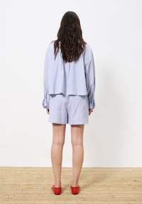 Übergroßes Shirt mit blauen und weißen Streifen und passender Shorts, mit lässigem Schnitt. Von hinten getragen mit roten flachen Schuhen.