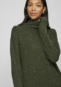 Maglione verde a maglia con colletto alto, caratterizzato da una texture morbida e maniche lunghe. Il design presenta una vestibilità rilassata con una silhouette ampia.