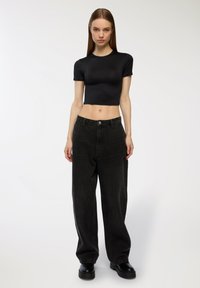 Czarny krótki t-shirt, wysoki dekolt, dopasowany krój. Spodnie dżinsowe w kolorze czarnym, wysokie w talii, luźne, z dużymi kieszeniami. Grube czarne buty na platformie.