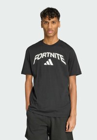 Sort kortærmet t-shirt lavet af bomuld med "FORTNITE" og Adidas-logo i hvid på forsiden. Løs pasform med rund halsudskæring.