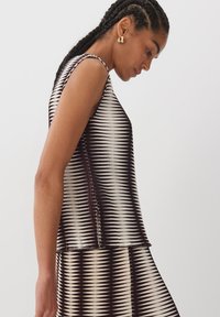 Top senza maniche con un motivo ondulato in nero e beige, realizzato in materiale leggero, caratterizzato da una forma leggermente svasata e dettagli con spacco laterale.