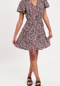 Robe fleurie avec un col en V, manches courtes à volants, taille cintrée et jupe évasée. Couleurs : noir, rose, blanc et vert.