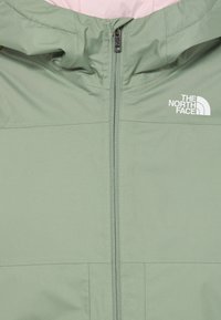 Hele roheline kapuutsiga jakk, millel on ees lukk ja valge "The North Face" logo rinnal, kaela juures on nähtav hele roosa vooder.