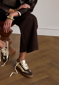 Sneakers with a brown and gold color scheme, featuring a mix of suede and leather textures, with cream laces and a rubber sole.