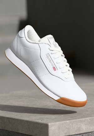 White sneaker with a smooth leather upper, shaped toe, rubber outsole, and light tan accents. Features lace closure and side branding.