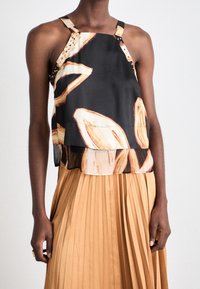 Haut noir sans manches avec motif abstrait beige, design superposé et bretelles décoratives uniques. Associé à une jupe plissée beige.