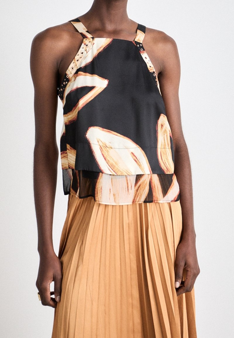 Haut noir sans manches avec motif abstrait beige, design superposé et bretelles décoratives uniques. Associé à une jupe plissée beige.