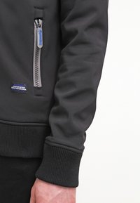 Svart sweatshirt med en slät yta, med en sidofack och ribbade cuffs. Inkluderar en märkeslapp på bröstet.