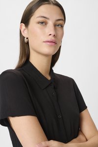 Camicia nera a maniche corte con chiusura a bottoni e colletto. Realizzata in tessuto testurizzato, presenta una vestibilità comoda. Design semplice e classico.