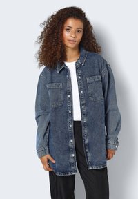 Camicia di denim di colore blu scuro, con chiusura a bottoni, due tasche sul petto e una vestibilità comoda con maniche lunghe e colletto.