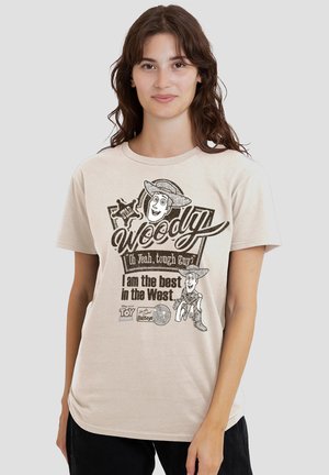 Woman wearing a beige T-shirt with black text and images of Woody from Toy Story, reading "Woody, Oh Yeah, tough guy? I am the best in the West."