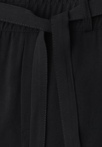 Gros plan d'un pantalon en tissu noir avec une taille élastique et une ceinture en tissu nouée au centre devant.