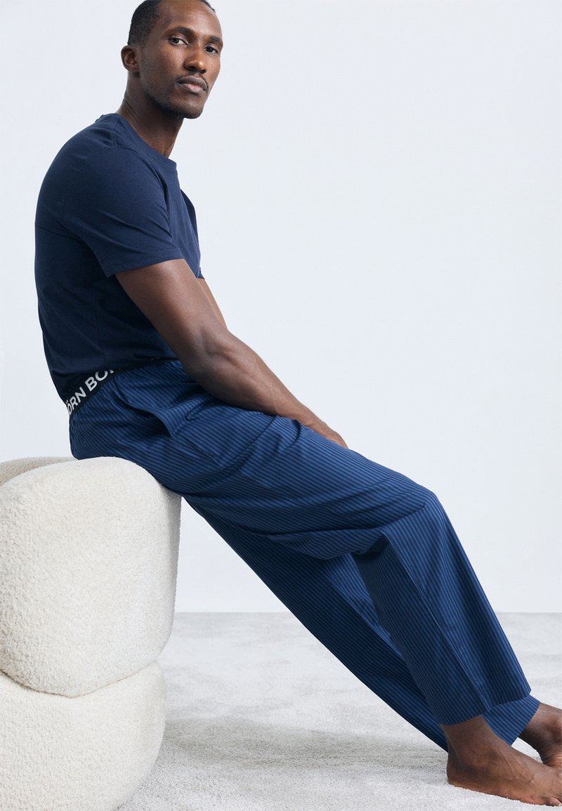 Mornarska majica i prugaste pidžama hlače u plavim tonovima. Hlače imaju brendirani elastični pojas i širok su kroj. Mekana tekstura.