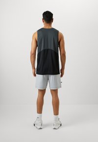 Sleeveless athletic tank top in dark gray and black, paired with light gray shorts. The tank features a color-blocked design and soft fabric.