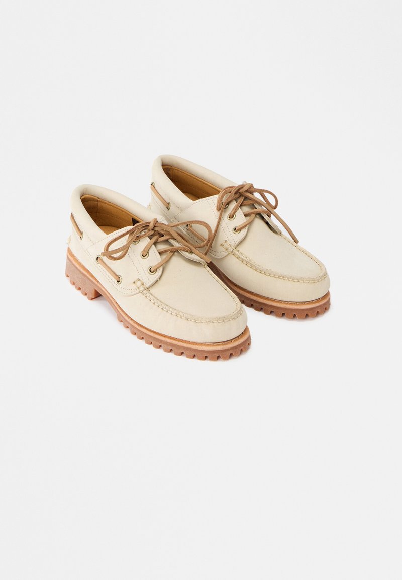 Μπεζ δερμάτινα παπούτσια τύπου boat με κορδόνια, καφέ λαστιχένιες σόλες, ραφές και επενδυμένους γιακάδες σε λευκό φόντο.