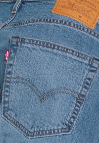 Poche arrière d'un jean en denim bleu avec l'étiquette rouge emblématique Levi's et un patch en cuir marron au-dessus de la ceinture.