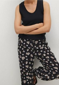 Haut sans manches noir associé à un pantalon ample imprimé floral sur fond sombre. Les pantalons présentent des fleurs blanches et beiges sur un tissu noir.