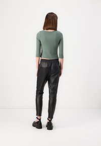Grønn tettsittende topp med trekvart ermer, kombinert med svarte bukser i imitert lær. Glatt tekstur og detaljer med elastisk midjebånd synlig.