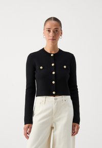 Black cropped cardigan with long sleeves, featuring gold buttons and two front pockets. Made from a knitted material with a smooth texture.