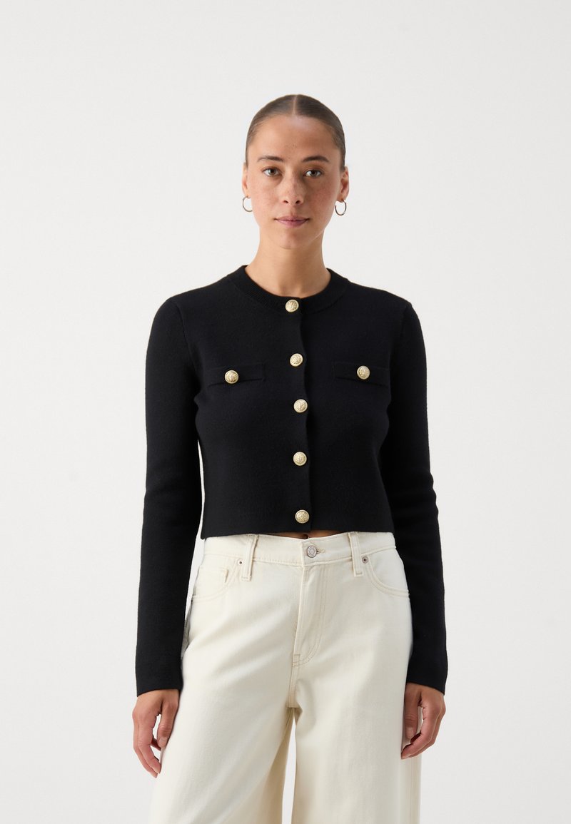 Black cropped cardigan with long sleeves, featuring gold buttons and two front pockets. Made from a knitted material with a smooth texture.