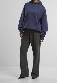 Sweat à capuche bleu marine avec une poche avant, associé à un jean gris foncé taille haute à jambes larges. Tissu lisse et coupe décontractée.