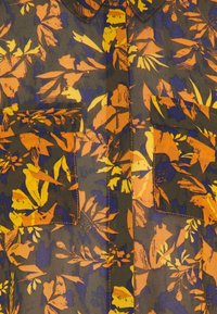 Camisa de manga corta con un patrón floral en naranja, amarillo y azul sobre un fondo oscuro, con dos bolsillos en el pecho y costuras en contraste.