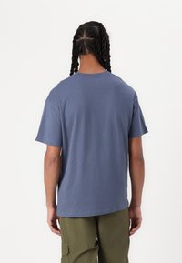 Tricou din bumbac albastru cu mânecă scurtă, cu o croială lejeră, guler rotund și textură netedă, purtat cu pantaloni cargo verzi măslinii.