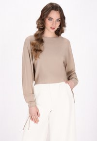 Maglia beige chiaro a maniche lunghe con tessuto texturizzato e vestibilità comoda, abbinata a pantaloni bianchi a gamba larga con dettaglio a laccio.