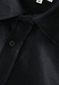 Zwarte linnen blouse met een kraag, enkel zwart knoopje en zichtbare stofstructuur. Maatlabel weergegeven als 'M'.