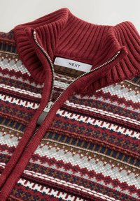 Maroon zip-up sweater with a ribbed collar, featuring intricate patterns in white, navy, and brown. Label reads 'NEXT'. Textured knit fabric.