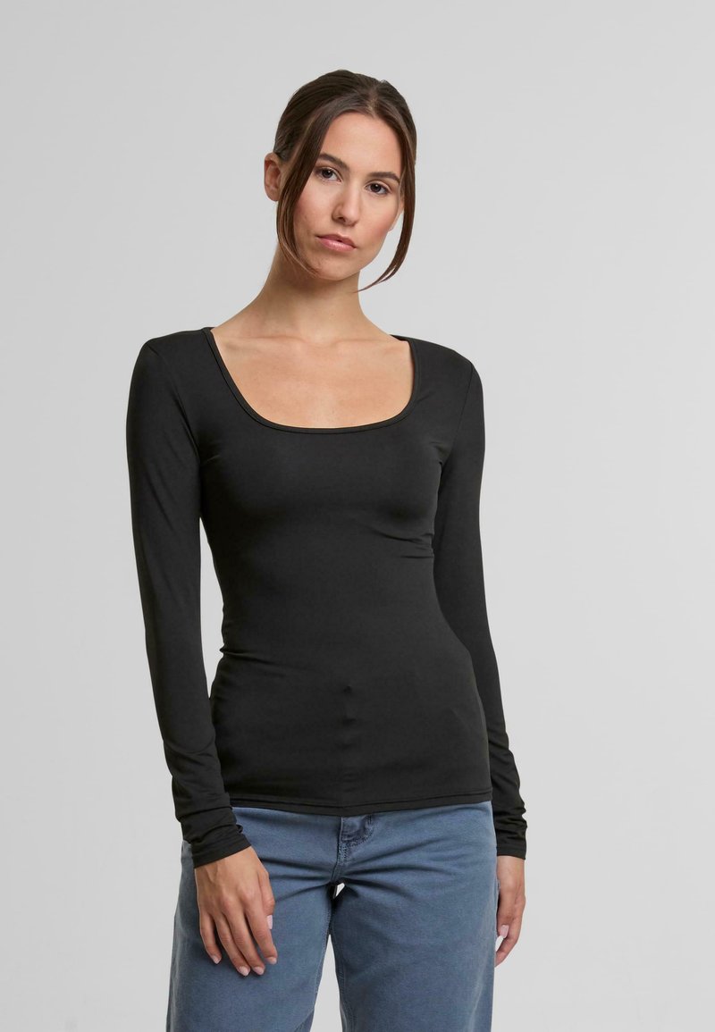 Černé tričko s dlouhým rukávem a kulatým výstřihem, přiléhavý střih, hladká textura a jemné detaily prošívání, v kombinaci s světle modrými džíny.