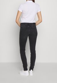 Černé slim-fit džíny s vysokým pasem, zadními kapsami a hladkým povrchem, spárované s bílým polo tričkem a bílými teniskami.