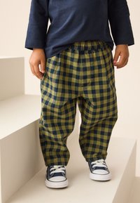 Temno modra majica z dolgimi rokavi, kombinirana z zeleno-modrimi karo hlačami z elastiko v pasu. Obleko dopolnjujejo bele superge.