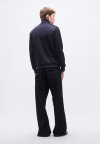 Φούτερ ναυτικού τύπου με ψηλό γιακά και ριμπ τελείωμα, συνδυασμένο με σκούρο τζιν παντελόνι φαρδύ στο κάτω μέρος με αντίθετη ραφή και λογότυπο στην πίσω τσέπη.