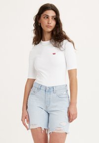 Hvid skjorte med korte ærmer og rund hals, der har et lille rødt Levi's-logo. Kombineret med lys blå slidte denimshorts.