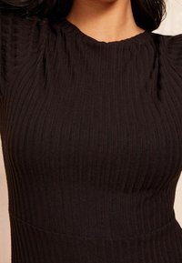 Robe noire côtelée avec un tissu texturé, une silhouette ajustée et un col rond avec de légers fronces aux épaules.