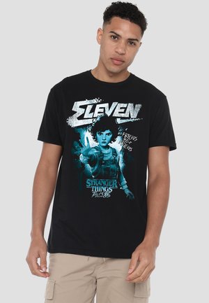Young man wearing black Stranger Things t-shirt featuring character Eleven with outstretched hand and text "Friends Help Friends."