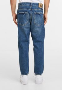 Sinisin denim farkut, rento malli, haalistunut tekstuuri ja kaksi takataskua. Viimeistelty brändilogo vyötäröllä.
