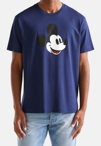 Námorně modré bavlněné tričko s velkou grafickou hlavou Mickey Mouse ve bílé a černé barvě ve středu, kulatý výstřih a krátké rukávy.