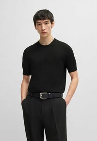 Black short-sleeve knit shirt with a round neck, paired with black tailored pants and a black belt featuring a silver buckle.