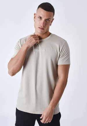 Camiseta de manga corta beige texturizada con cuello redondo, que presenta un sutil logotipo en el pecho y un diseño ajustado.