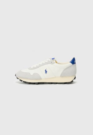 Sneaker grigia e bianca realizzata in materiali scamosciati e di tela, con un tacco di accento blu, lacci bianchi e una suola nera texturizzata. Logo sul lato.