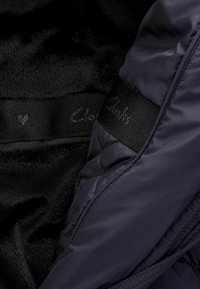 Giacca imbottita blu navy con un morbido rivestimento in pile nero. Presenta un'etichetta in tessuto nero con "Clarks" in argento e un piccolo dettaglio a forma di cuore.