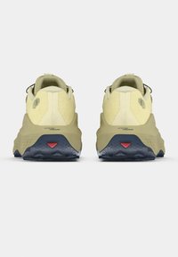 Παπούτσια για τρέξιμο σε μονοπάτια σε ανοιχτό κίτρινο και ελιά, με υφασμάτινο επάνω μέρος, ενισχυμένη φτέρνα και ανθεκτική μαύρη εξωτερική σόλα με κόκκινη λεπτομέρεια.